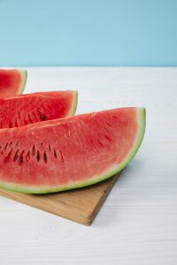 A watermelon with a large knife on top of a wooden cutting board